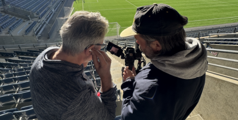 To menn ser inn i et kamera og lytter gjennom et headset. 