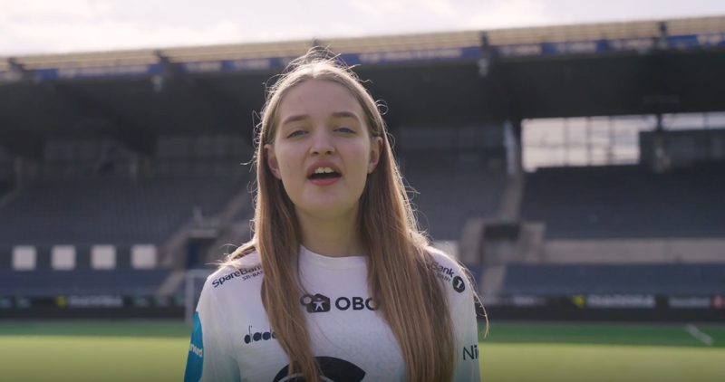 Ung jente sier "aaaa" og ser inn i kamera. Har på seg vikingdrakt, og står midt på banen. 