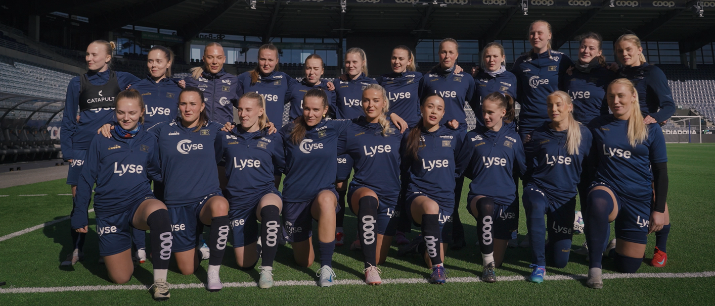 Kvinnelag ikledd vikingdrakt står på banen og synger inn i kamera.