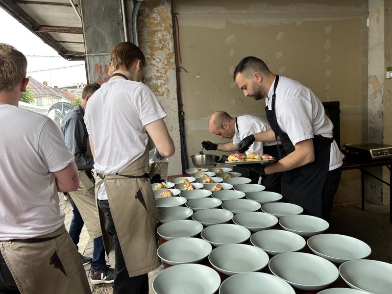 Kokker står på rekke og rad og danderer mange tallerkener. 