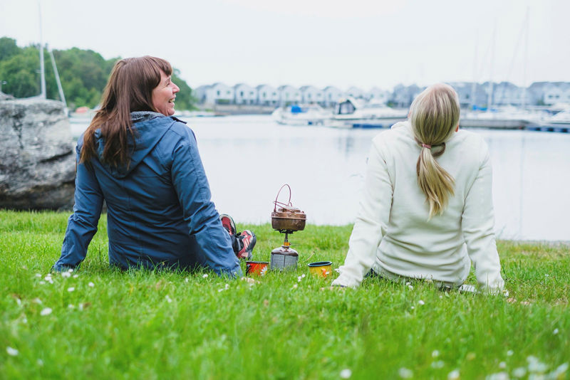 To lattermilde kvinner sitter på gresset i Grønnavigå med primus. Foto: John Petter Nordbø, Turistforeningen