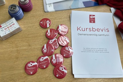 Røde klistremerker og buttons på et bord. Det står demensvennlig på dem.