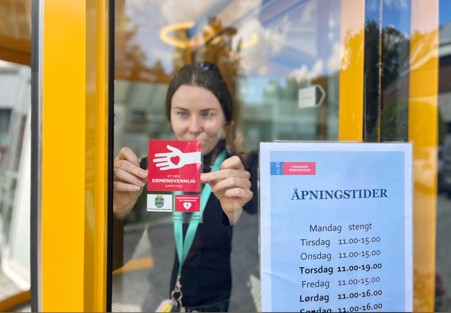 Barbara Slowik som klistrer opp merket demensvennlig samfunn på inngangsdøren på kunstmuseet.