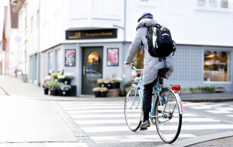 Vi ser en eldre kvinne på en damesykkel som sykler oppover Museegaten, forbi blomsterbutikken. 