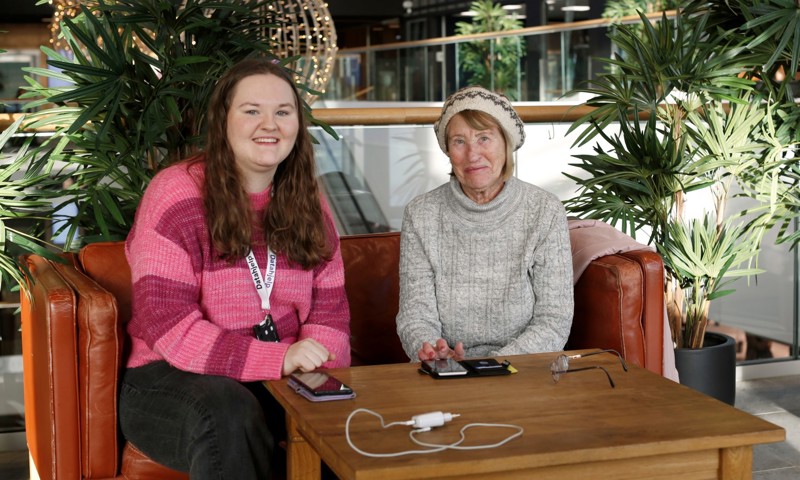Jenney Helseth og Ingerlin Birkeland Rage som sitter i en sofa. de har et bord foran seg hvor det ligger to smarttelefoner. 