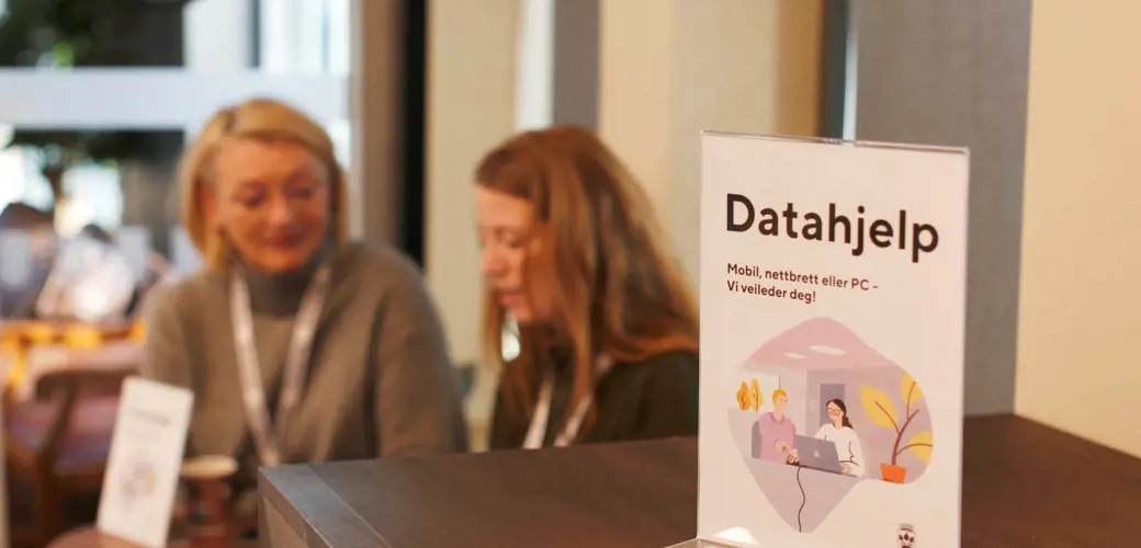 God synlighet i lokalene er viktig, noe som gjør terskelen lavere for å spørre om hjelp.  Bildet viser et skilt som det står datahjelp på. Det står på en vindusbenk, og i bakgrunnen ser vi at Tone Hafnor og Elin Halvorsen sitter.