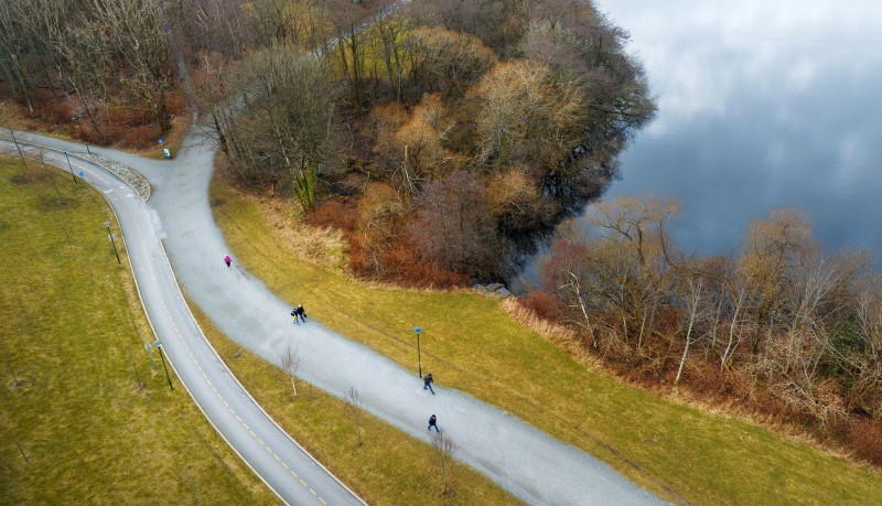 Vi ser utsnitt av et turområde langs Mosvannet fra luften. Det er sen høst med litt brunt og gule farger i vegetasjonen. På de to stiene avbildet skimter vi folk som går tur.