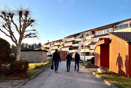 Vi ser Mjughaug terrasse fra forsiden, med gangveien hvor vi ser tre av naboene som går på veien.