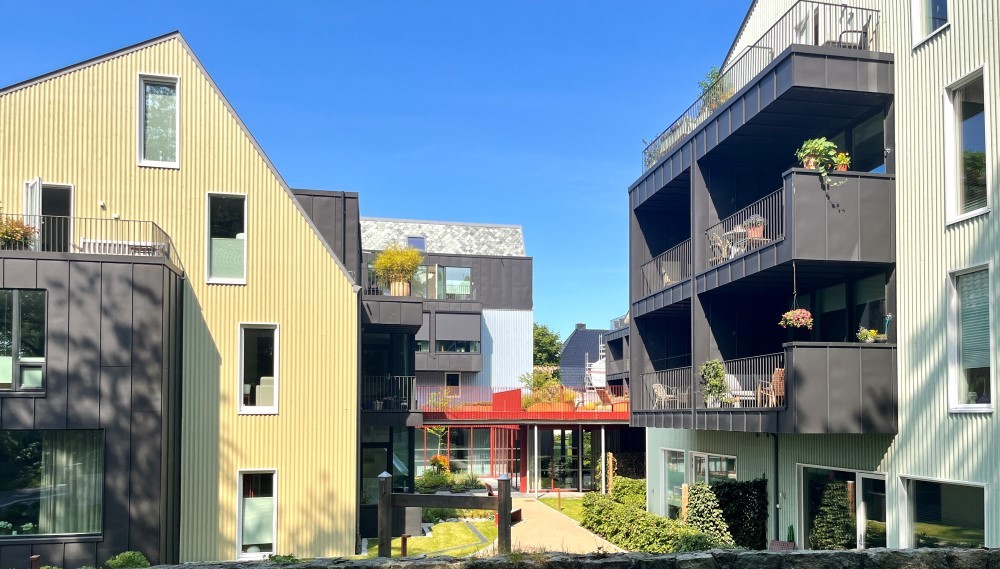 Bildet viser to av husene på Vålandstun, med balkonger, store vinduer og hage i mellom. VI ser at husene er forbundet med hverandre. 