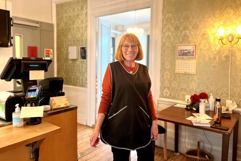 Vi ser Inger Paulsen som står blid og fornøyd i forkle foran disken. 