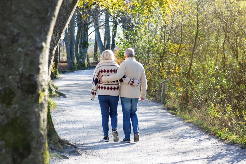 Bildet viser et par, kvinne og mann som går tett sammen. De går tur på en grusvei. 