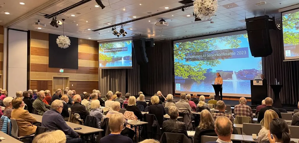 Bildet viser konferansesalen med mange mennesker som følger med på åpningen av Seniorkonferansen 2023 som skjer fra scenen.