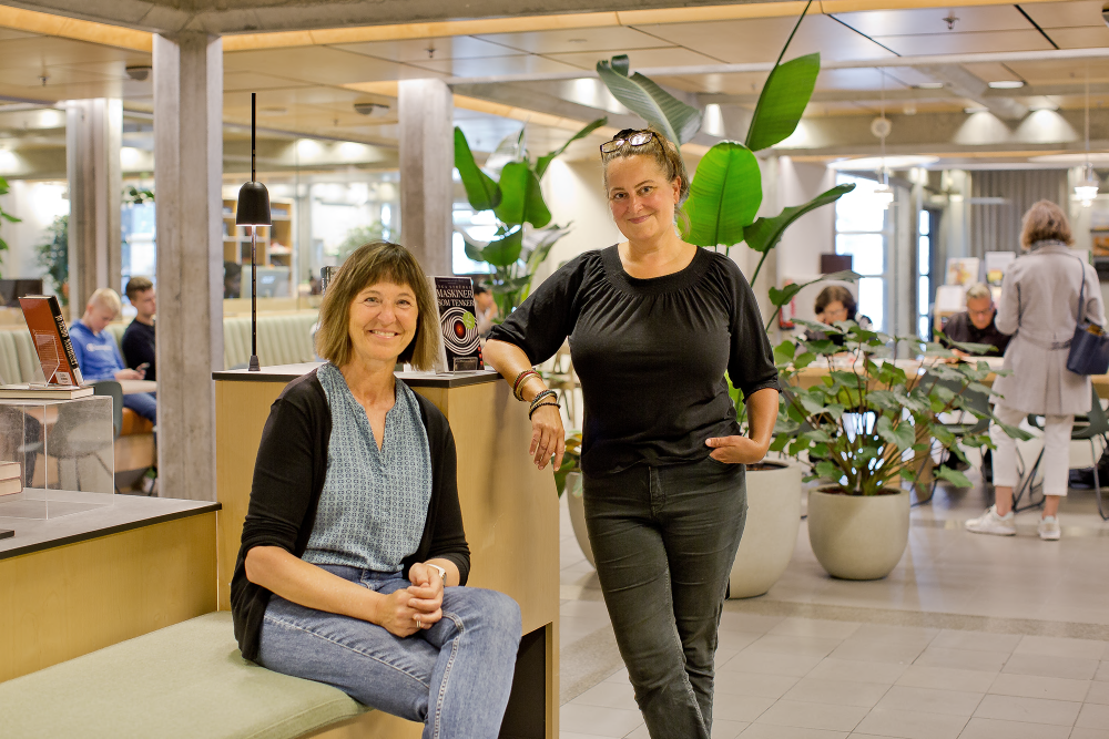 Vi ser de to ansatte på Sølvberget som står, og en sitter blant benker og bøker i første etasje. I bakgrunnen ser vi flere mennesker som sitter ved bord og leser og snakker.