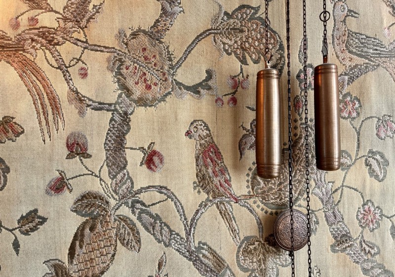 Bildet viser deler av veggen, med vevd tapet i stoff. Fargen er gul/gull og i bruntoner. Med fugler som  sitter på grener.