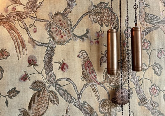 Bildet viser deler av veggen, med vevd tapet i stoff. Fargen er gul/gull og i bruntoner. Med fugler som  sitter på grener.