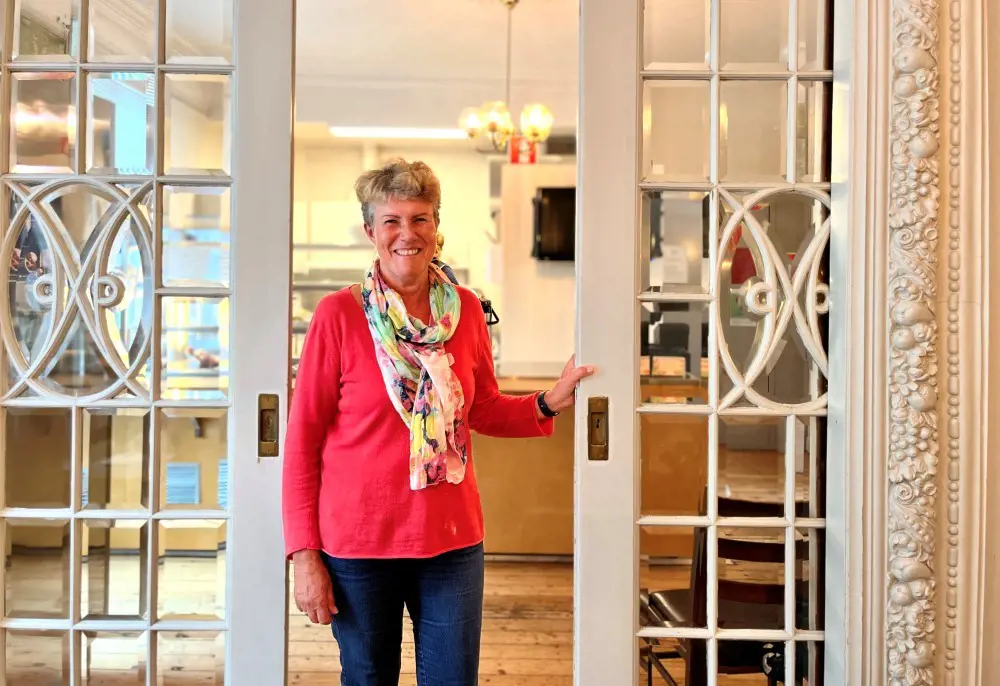 Brit Bjørkli ønsker deg velkommen til Tante Emmas Hus. Vi ser et bilde Brit Bjørkli som driver Tante Emmas Hus. Hun står i døråpningen inn til kafeen.