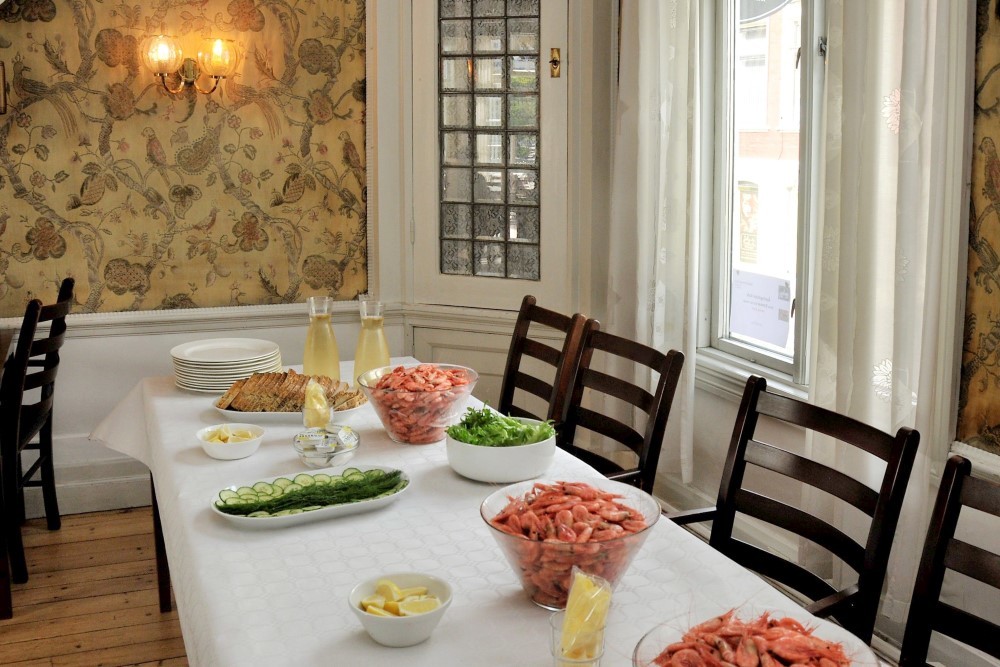 Bildet viser et oppdekket bord med hvit duk, og skåler med reker, brød og tilbehør. Det er rekefest på Tante Emmas HUs.