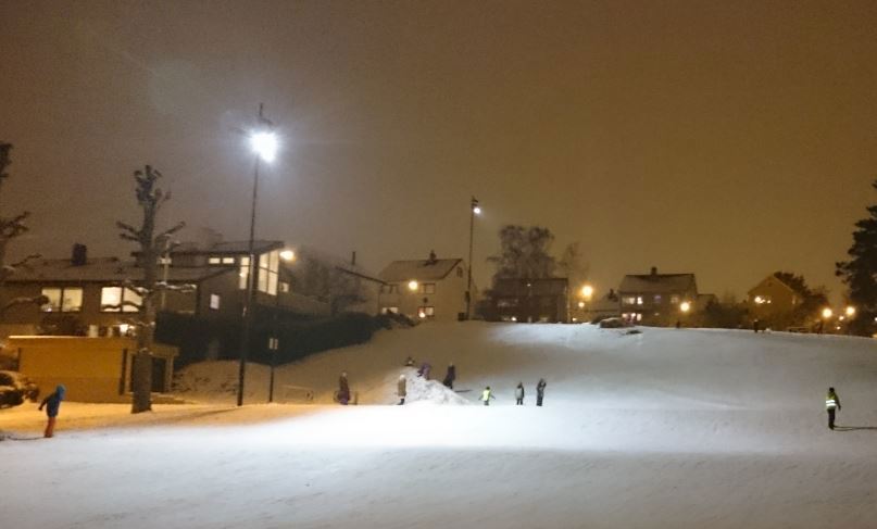Akebakken på sørsiden av Vålandshaugen. (Foto: Rune J Thingdal) Akebakke i mørket, med flombelysning og noen barn som aker