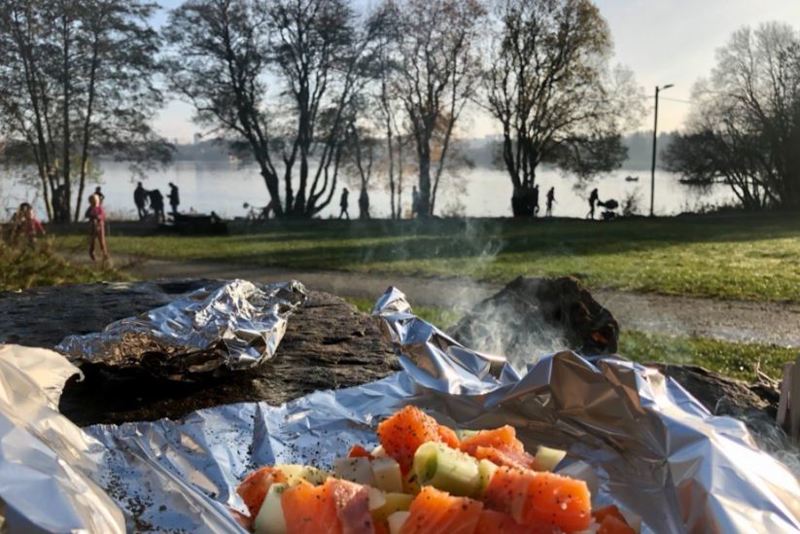 Grillmat på folie i forgrunnen, folkeliv på turstien langs vannet i bakgrunnen