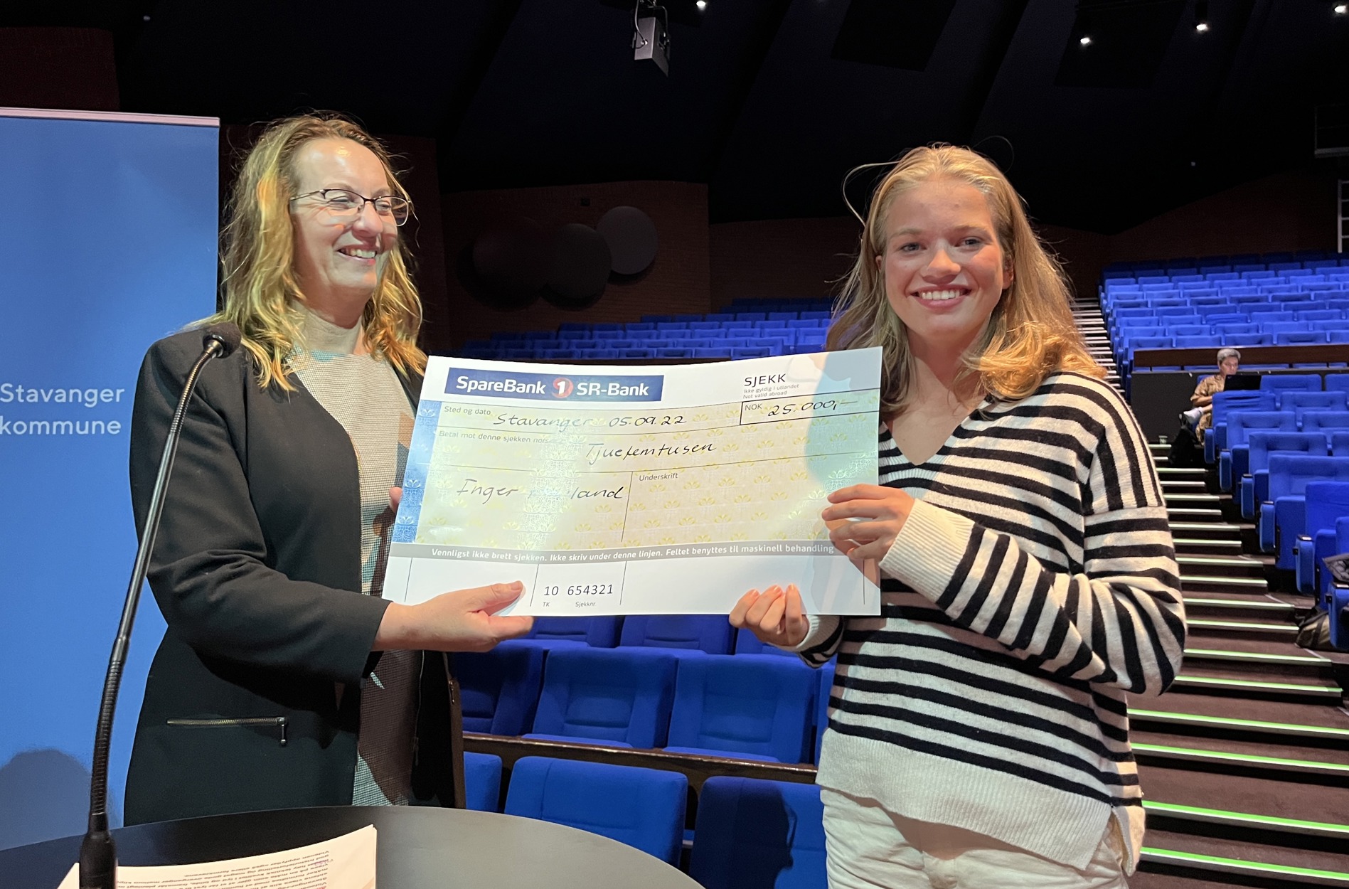 Inger Hovland mottar premiesjekk for førsteplass i videokonkurransen ungsiddis. Overrekkes av fungerende ordfører Dagny Sunnanå Hausken under et kommunestyremøte.