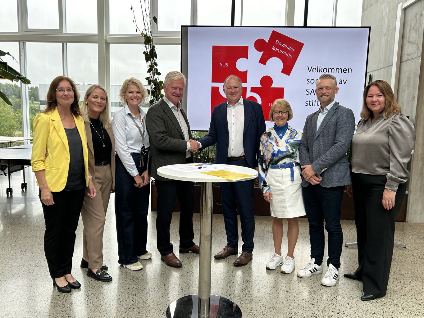 PARTNERE I SAFER: Fra v. Bjørg Oftedal, prorektor undervisning UiS, Lena Heimvik, klinikksjef prehospital klinikk SUS, Elsa Søyland, CEO SAFER, Tore Lærdal styreleder SAFER, Per Kristian Vareide kommunedirektør Stavanger kommune, Eli Karin Fosse tidligere direktør helse og velferd Stavanger kommune, Helge Dragsund, kommunalsjef helse og omsorg Stavanger kommune og Stina Løkke, direktør i helse og velferd Stavanger kommune. Åtte representanter for UiS, SUS, Stavanger kommune og SAFER står skulder ved skulder bak et rundt bord der avtalen ble signert.