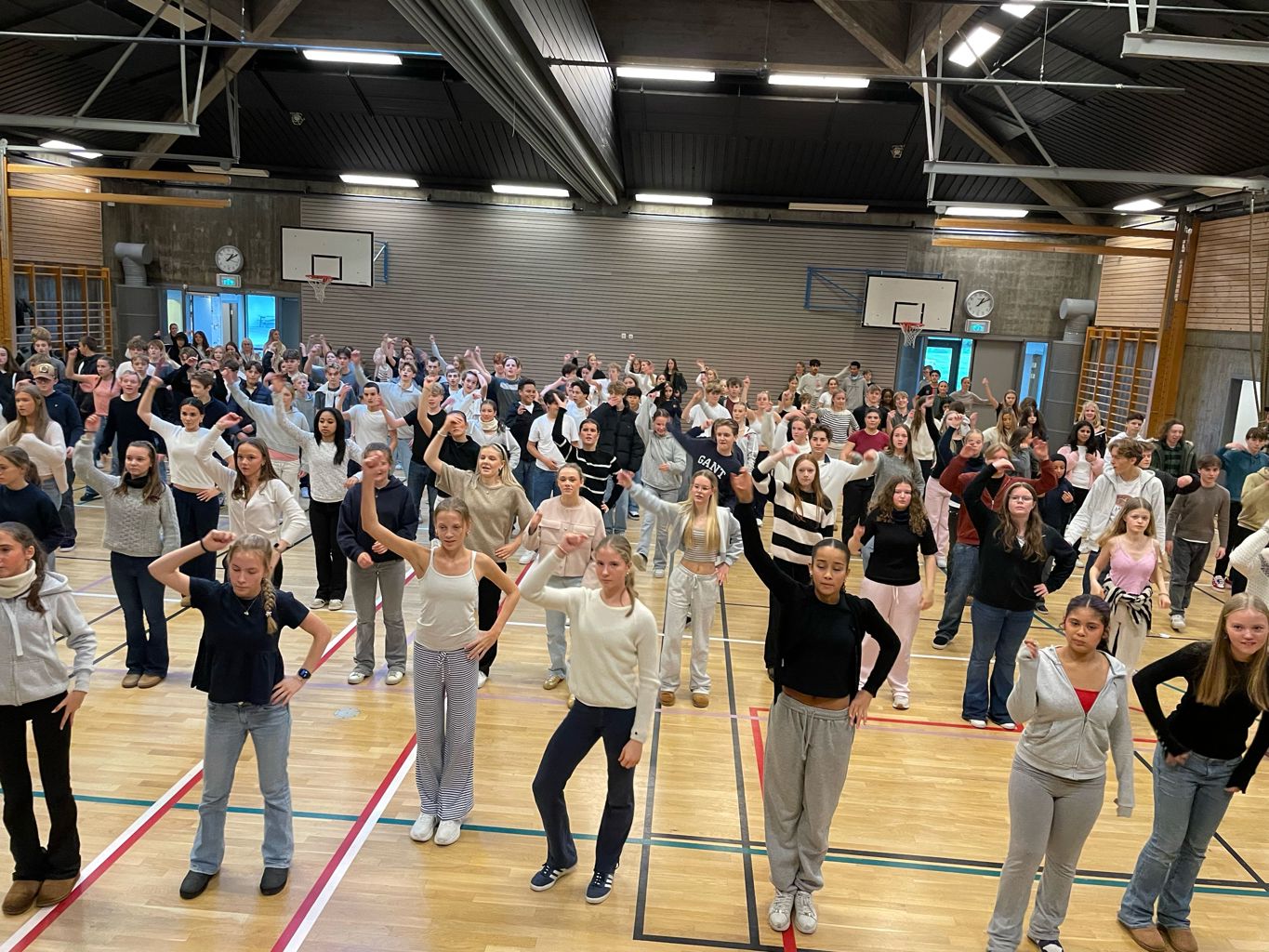 ØVER: Elevene på 9. og 10. trinn på Gosen skole er i gang med øvinger til jubileumsrevyen som har premiere i januar 2025. Bildet viser skolens gymsal full av elever som står med høyre arm opp i været i forbindelse med øvelse.