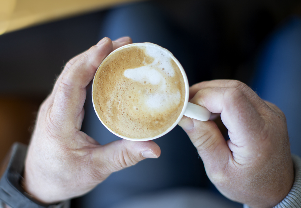 Gamle hender holder rundt en kopp med kaffe.