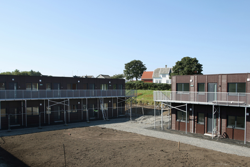 To rader med mørke brune modulbygg med uteplass i midten.