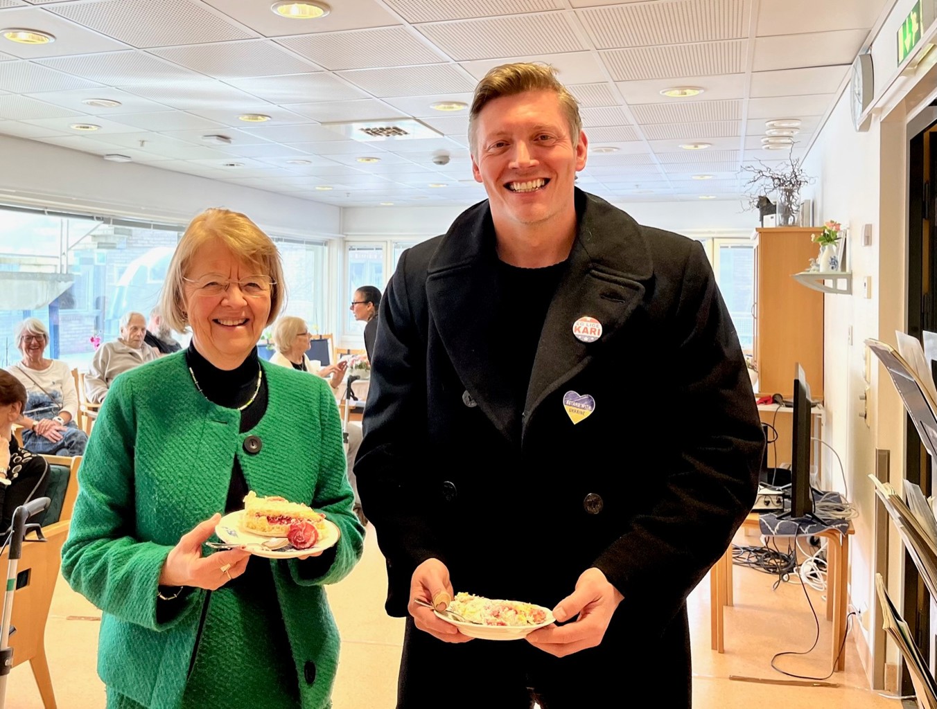Eli Karin Fosse, direktør for helse og velferd og Dag Mossige, leder for utvalg for helse og velferd feiret fredag nytt varslingssystem på Tasta sykehjem. På bildet ser vi Eli Karin Fosse, direktør for helse og velferd, og Dag Mossige, leder for utvalg for helse og velferd som spiser kake, og smiler fornøyd til fotografen.