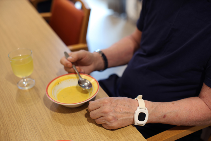 En mann som sitter ved et bord og spiser. Vi ser armene. 