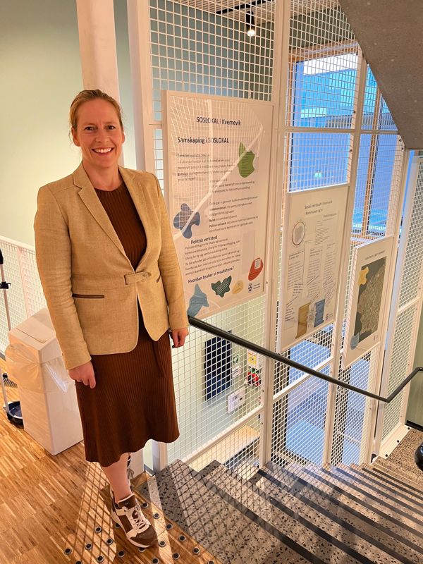 Christel Dahl foran tre innrammede plakater. Var du en av de mange som svarte på spørreundersøkelsen våren 2022, eller deltok du på fokusgrupper eller bylab? En oppsummering av resultatene henger i trappa på bydelshuset i Kvernevik. 