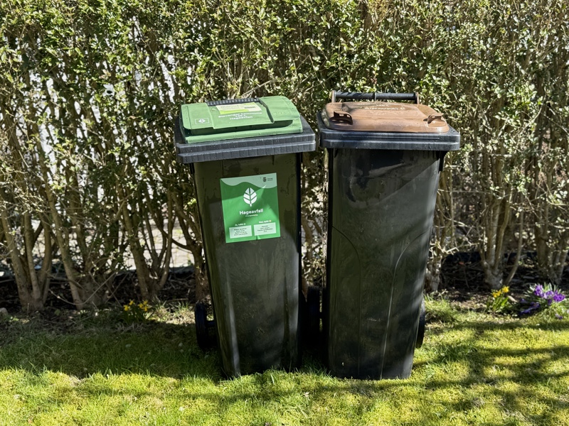 To svarte beholdere, en med grønt lokk for hageavfall, en med brunt lokk for matavfall.