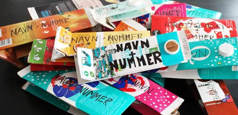 Brettet drikkekartong, der navn og nummer er skrevet på med tusj