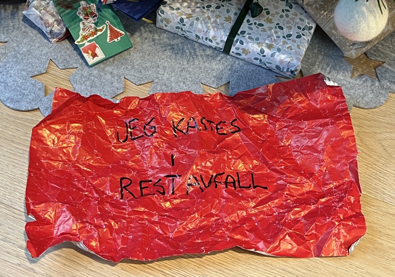 Julepapir under juletreet med beskjeden "jeg kastes i restavfallet"