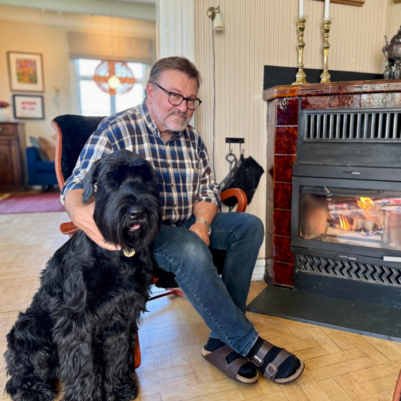 Hund og mann i stol ved fyr i peisen.