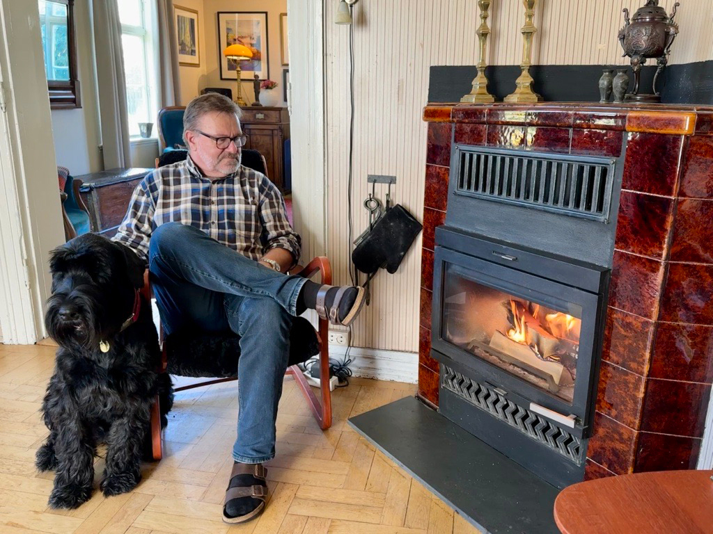 Mann og hund ved peis i stua