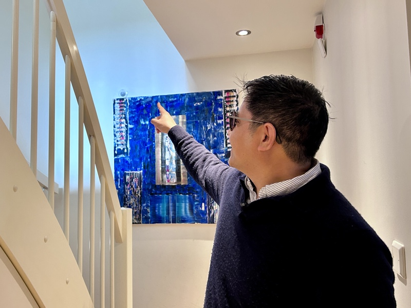 En mann med blå genser med blå skjorte under peker på en hvit vegg med et blått bilde på. Rett over trappen tenker han å henge opp en varmepumpe.