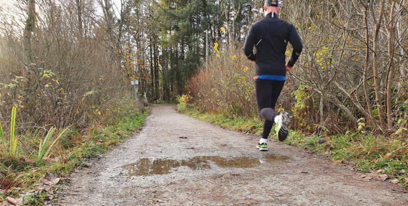 Mann som jogger over en pytt på en slitt grusvei