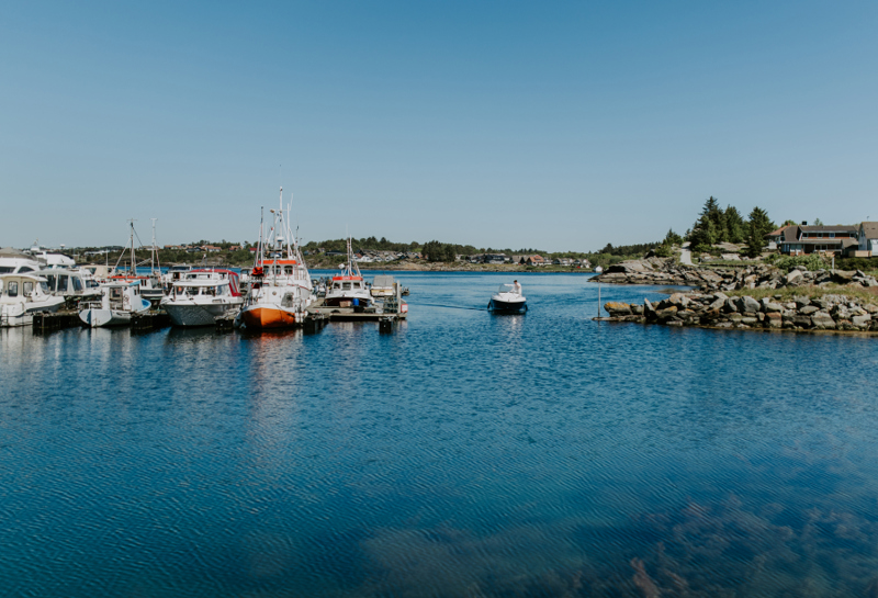 Flere båter som ligger fortøyd i båthavnen og en båt som kommer kjørende inn på vannet