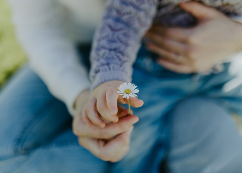 Hender til mor og barn som holder i en hvit blomst