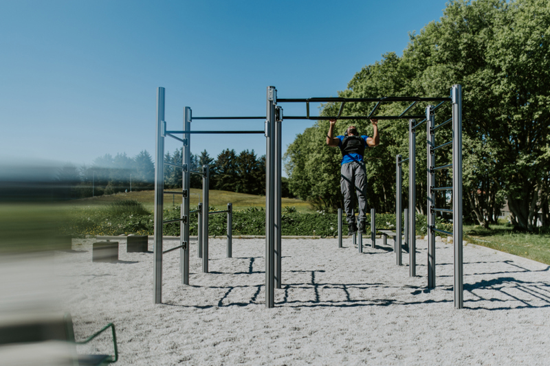 En mann trener styrke på utendørs klatre-/treningsapparat. 