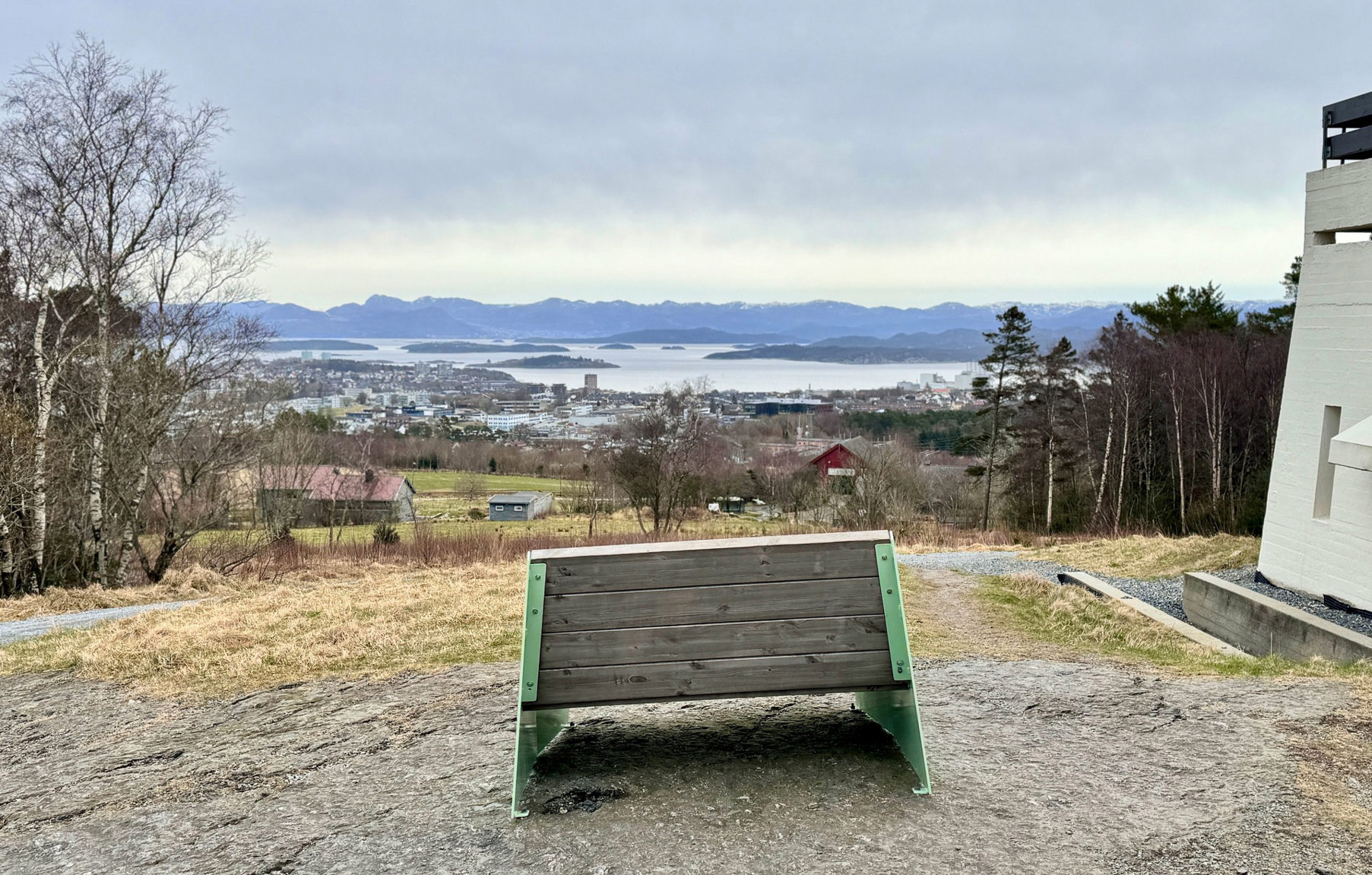 Benk oppe på en høyde, med utsikt over by, fjord og fjell.