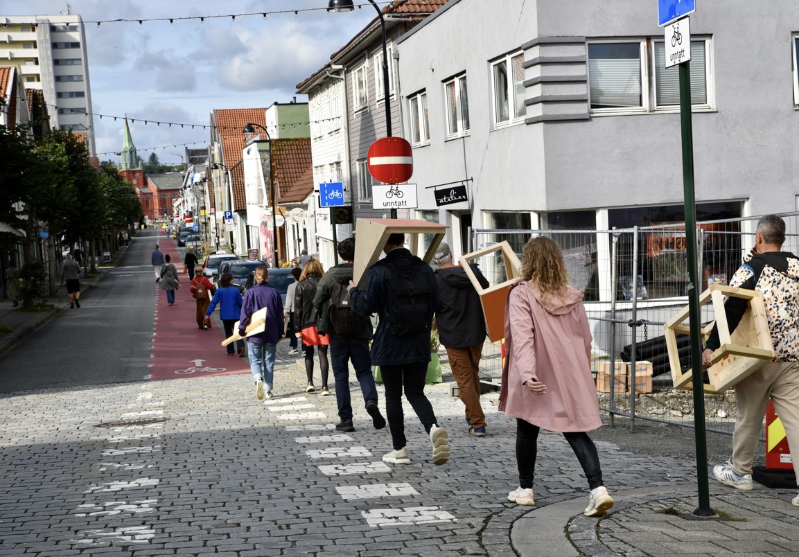 En rekke mennesker som går i et bymiljø og bærer på tre-konstruksjoner.