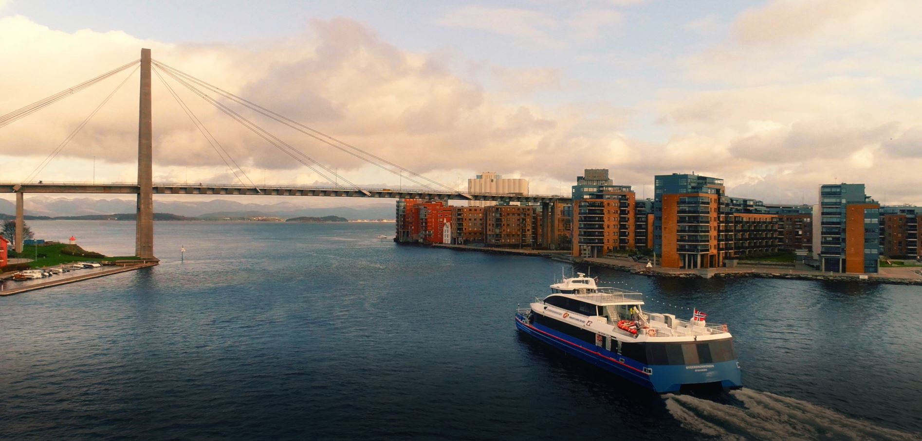 Bilde av en Rødnebåt som kjører under bybroen i solnedgang,