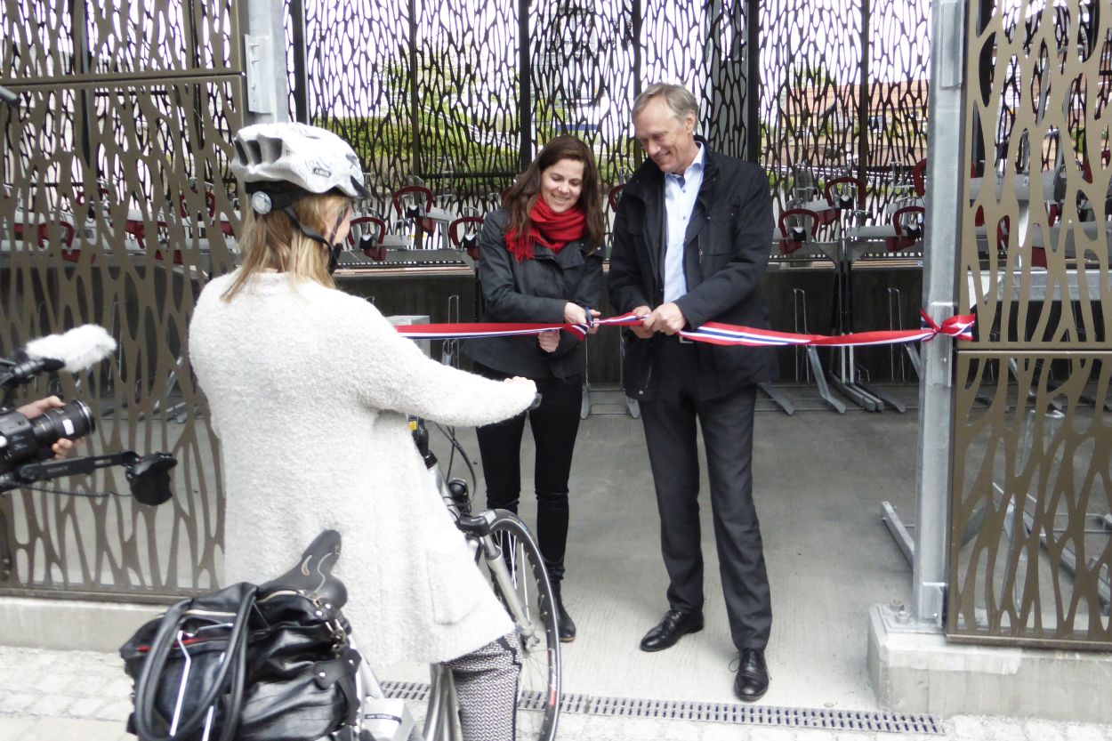 En dame og en mann klipper en snur for å åpne Asker sykkelhotell. En syklist står klar for å komme seg inn i sykkelhotellet for å parkere der.