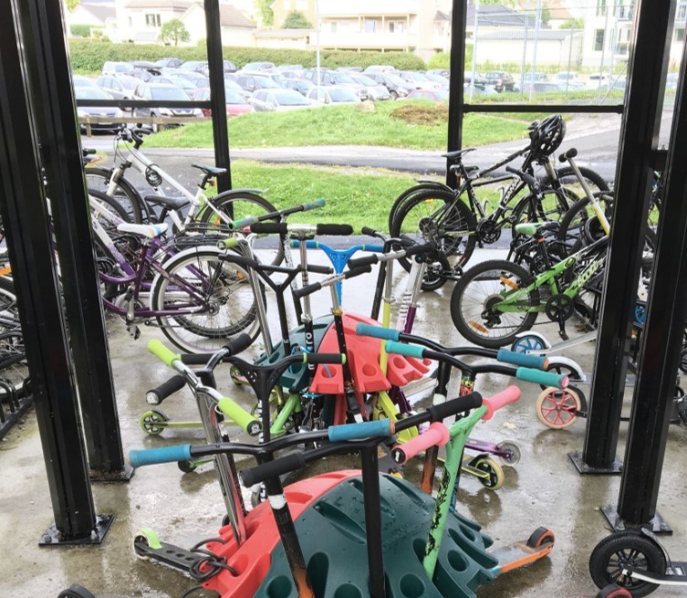 I en sykkelgarasje med glassvegger står barnesykler parkert i sykkelstativer og sparkesykler i sparkesykkelstativer.