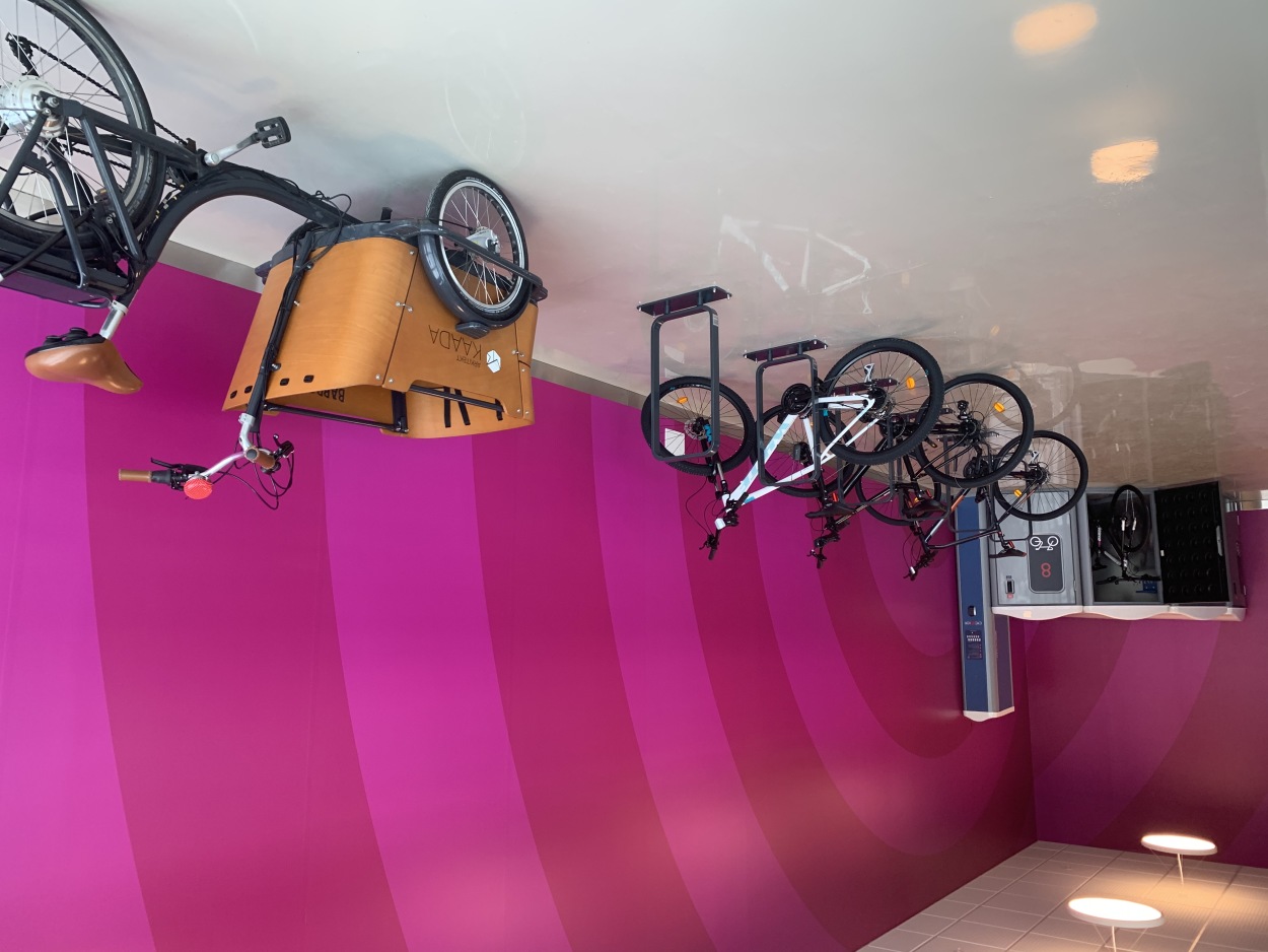 Bilder viser et innendørs sykkelparkeringsanlegg med sykkelbokser, stativer og oppstillingsplass til sykkelvogn