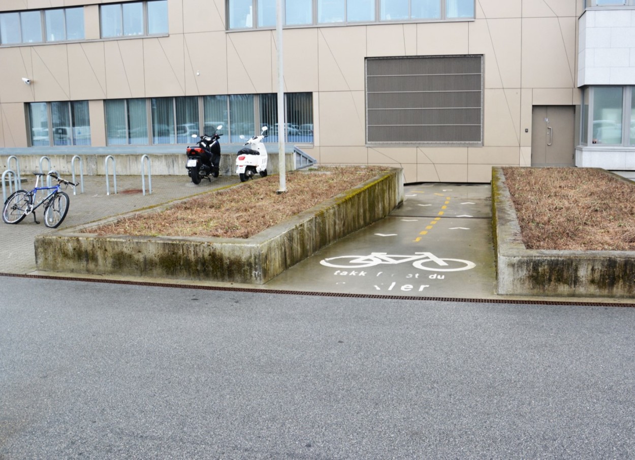 Foran kontorbygget til Aker solutions finnes det sykkelstativer til gjesteparkering. Veien til innendørsparkering er tydelig markert med tekst og figur i veiflaten foran bygget.