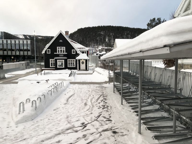På en untendørs sykkelparkeringsplass ligger det mye snø mellom stativene uten overdekk mens de toetasjes stativer som har overdekk er tilgjengelig og kan brukes.